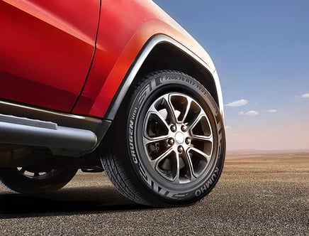 Close-up of a car tire and alloy wheel on a red vehicle, parked on an expansive paved surface under a blue sky.