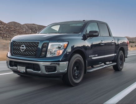 A black Nissan Titan V8 truck driving on a road with mountains in the background.