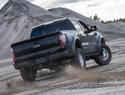 A black Ford F-150 Raptor driving on a dirt road with hills in the background.