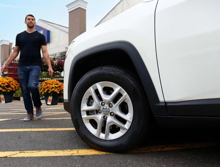 Man carrying potted flowers near a white car's tire in a parking lot.