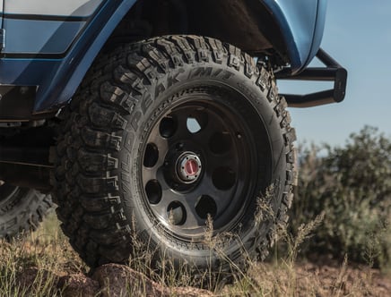 Close-up of an off-road vehicle's tire, a Falken Wildpeak M/T with rugged tread, on a grassy terrain.