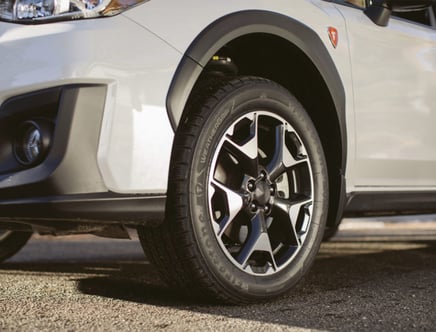 Close-up of a car's front wheel and bumper in a parking area.