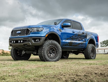 Blue lifted pickup truck parked on grass under cloudy sky.