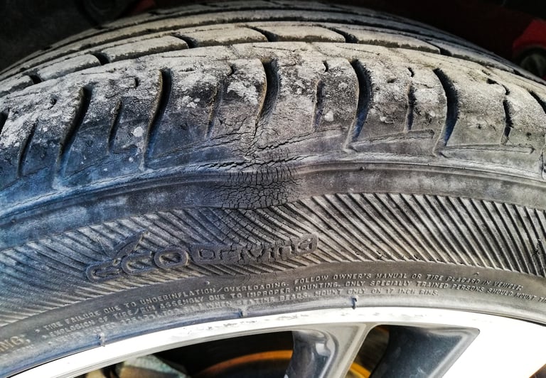 A worn and cracked car tire with visible tread pattern and sidewall bubble.