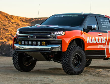 A customized off-road truck with Maxxis Tires branding, featuring a lifted suspension and large, rugged tires, parked on a desert landscape.