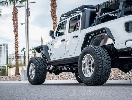 Customized white Jeep Gladiator with large off-road tires and aftermarket accessories parked on a street.