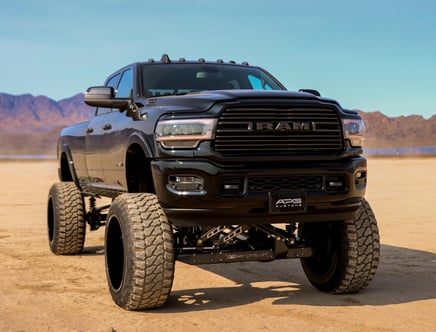 Lifted black Ram truck with large off-road tires in a desert landscape.