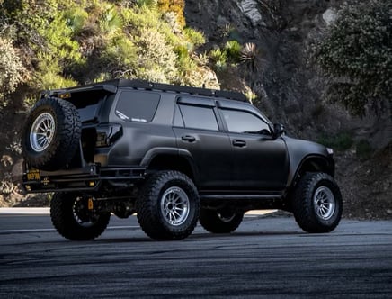 A black, heavily modified SUV parked on a mountain road with rugged terrain in the background.