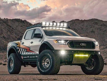 Customized Ford pickup truck with off-road modifications, including large tires and roof lights, set against a rocky desert backdrop with cloudy skies.