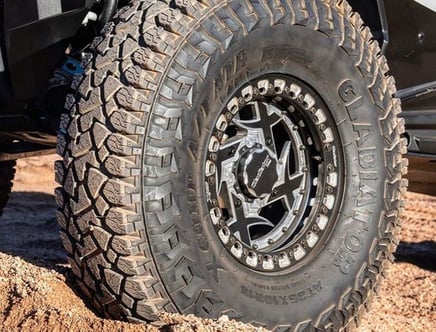 A large off-road tire with the brand name "Gladiator" visible on the sidewall, partially embedded in sand.