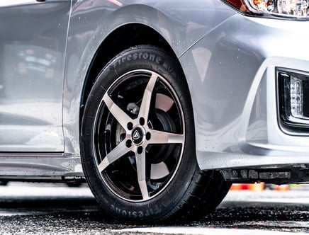 Close-up of a silver car with Firestone tires and black alloy wheels.