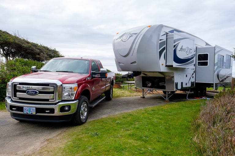 A red Ford truck parked next to a large Arctic Fox fifth-wheel trailer in a grassy campground.