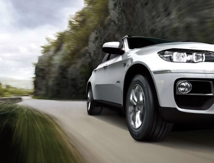 A silver SUV driving on a winding road with blurred greenery in the background.