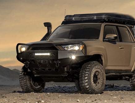 Modified off-road SUV with a roof rack and snorkel, parked on rocky terrain at dusk.