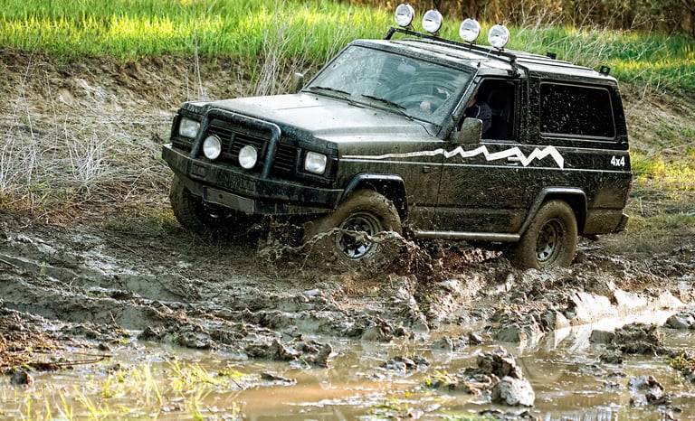 A black off-road vehicle covered in mud driving through a muddy terrain.