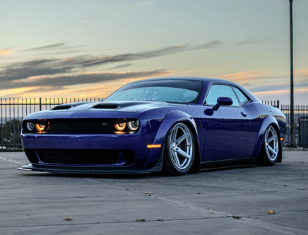 A low-angle shot of a purple sports car with custom alloy wheels, set against a sunset sky.