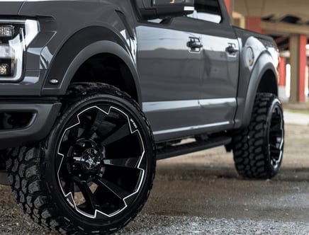 Front view of a grey pickup truck with large black off-road tires and rims.