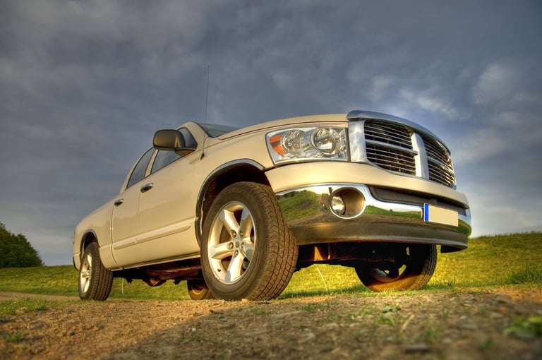 White pickup truck parked on a grassy terrain under a cloudy sky.