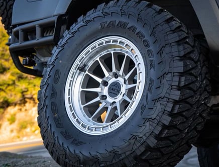 Close-up of a vehicle's off-road tire with "Arroyo Tamarock M/T" text and a detailed metallic wheel rim design.