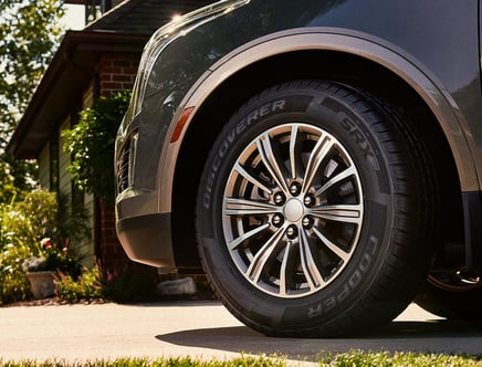 Close-up of a Cooper Discoverer SRX tire on a vehicle parked in a driveway beside a house.