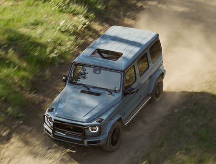 Blue SUV driving on a dirt road surrounded by greenery.