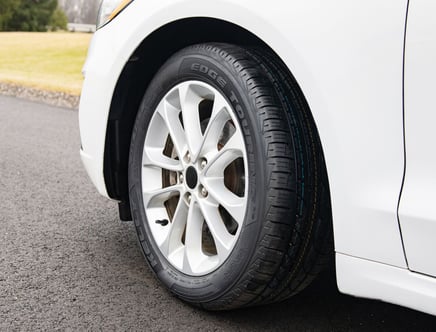 Car tire on a white vehicle parked on a paved road.