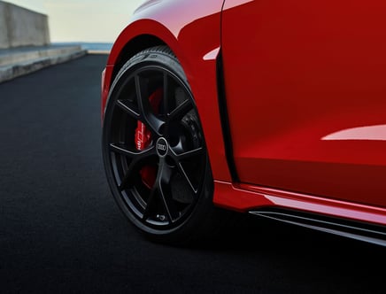 Close-up of a red car's front wheel with black rims and a red brake caliper featuring the Audi logo.