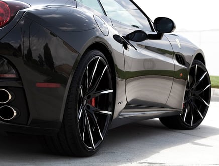 Shiny black sports car with large black alloy wheels, rear exhausts, and sleek design, parked on a road.