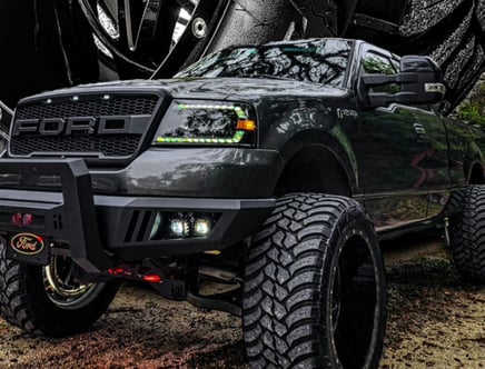 A lifted black Ford truck with off-road tires and custom grill.