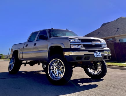 A lifted silver pickup truck with large chrome wheels parked on a residential street.