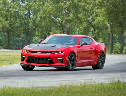 A red sports car with a black hood driving on a curved road with trees in the background.