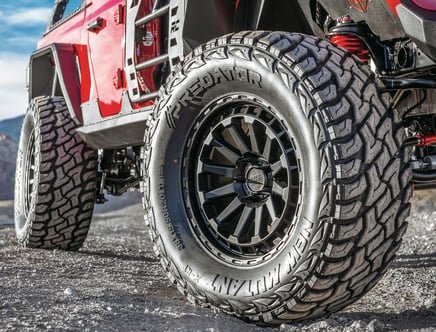 Close-up of a red off-road vehicle with large, rugged Predator tires on a dusty terrain.