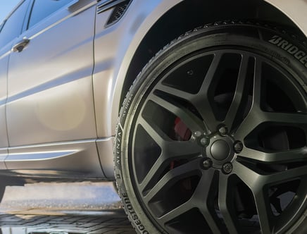 Close-up of a car's matte black alloy wheel and tire with a portion of the vehicle's silver body visible.