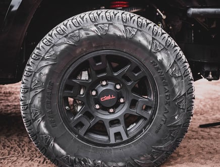 Close-up of a black off-road tire with aggressive tread pattern and a black matte wheel rim featuring red accents.