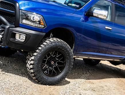 Blue pickup truck with off-road tires parked on gravel.