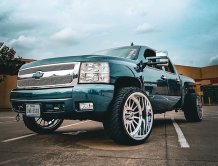 A customized blue pickup truck with large silver rims and a Texas license plate parked in an open area.