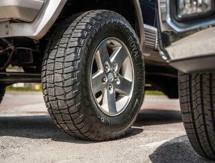 Close-up view of a vehicle tire with treads on a paved surface.