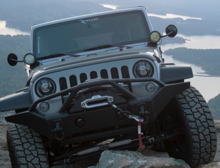 Off-road vehicle on a rocky terrain with a lake and forested landscape in the background.