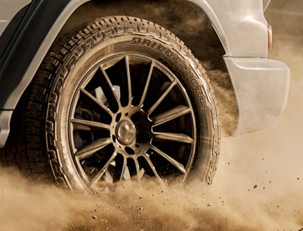 Close-up of a vehicle tire driving through dust, with "Bridgestone" visible on the sidewall.