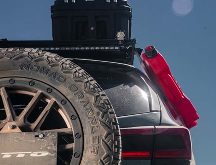 Close-up of a vehicle with a Nomad Grappler tire, rooftop storage, and a red fuel canister mounted on the back.