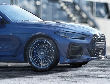 Blue sports car front view with shiny Vredestein wheels and large grill.