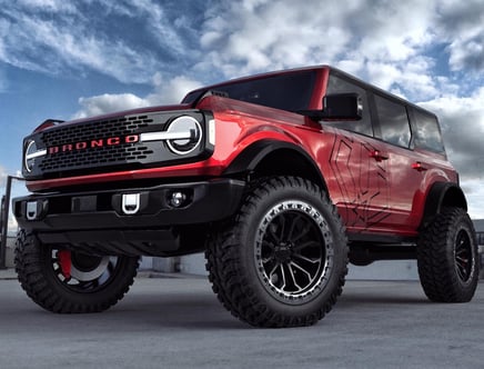 Red Ford Bronco with large off-road tires against a cloudy sky backdrop.