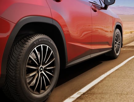 Close-up of a red car's rear tire and wheel on a road.