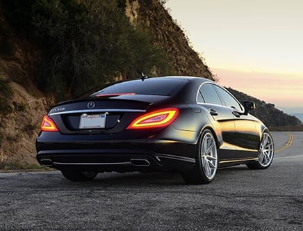 A black luxury sedan parked on a scenic mountain road at sunset.