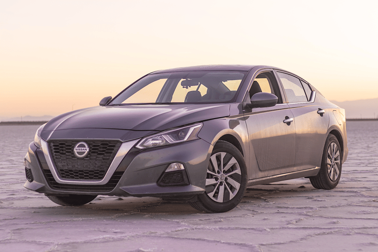 A gray Nissan sedan parked on a salt flat during sunset.