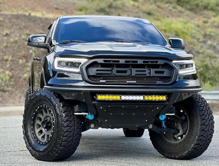 Modified black Ford pickup truck with large off-road tires, custom grille, and LED light bar.