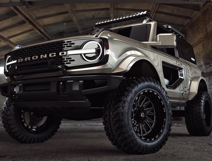 A rugged, customized Ford Bronco with off-road tires and a distinctive grille parked indoors.