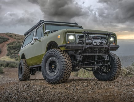 A rugged off-road vehicle with large tires and a front winch parked on a rocky path during rainy weather.