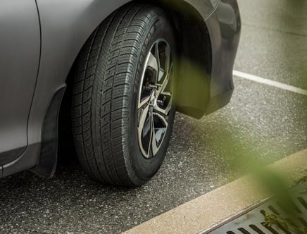 Close-up of a car tire on a gray vehicle parked on asphalt.