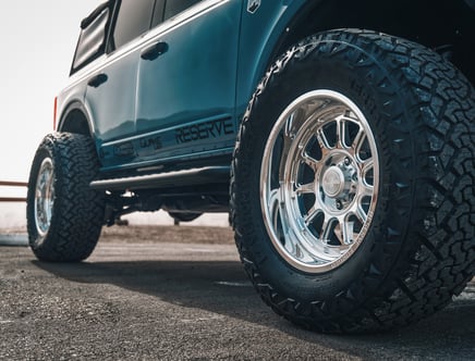 Close-up of a truck with large, rugged tires and chrome wheels parked on a paved surface.